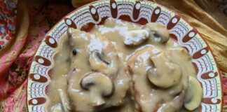 Δύο χρυσαφένιες χοιρινές μπριζόλες με πλούσια καφέ σάλτσα μανιταριών και φρέσκα μυρωδικά σε ένα λευκό πιάτο.