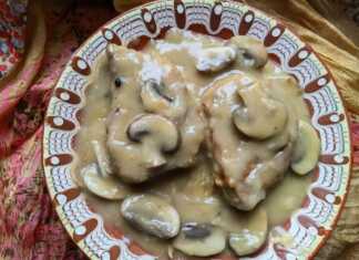 Δύο χρυσαφένιες χοιρινές μπριζόλες με πλούσια καφέ σάλτσα μανιταριών και φρέσκα μυρωδικά σε ένα λευκό πιάτο.