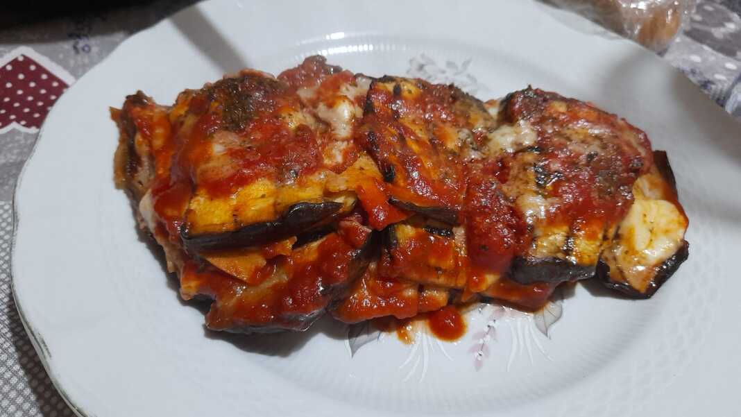 melitzanaParmiziana1 Μια φέτα από ψητές μελιτζάνες με ντομάτα και τυριά σερβιρισμένη σε πιάτο.