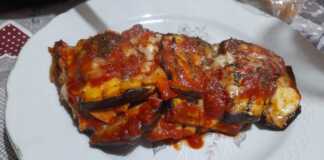 Μια φέτα από ψητές μελιτζάνες με ντομάτα και τυριά σερβιρισμένη σε πιάτο.