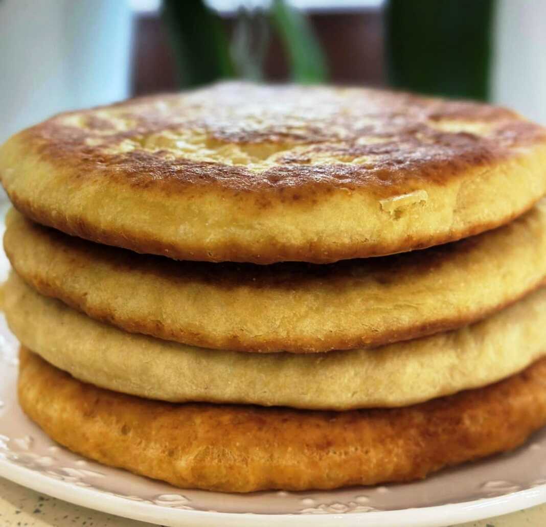 Στοίβα από αφράτες και χρυσαφένιες πίτες στο τηγάνι με κεφίρ, με λιωμένο βούτυρο να τις καλύπτει.