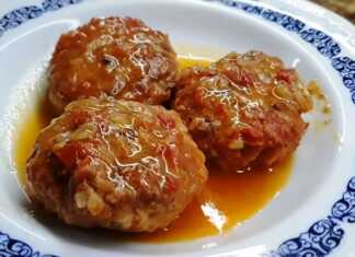 Ενα πιάτο με στρογγυλά, ροδοκοκκινισμένα κεφτεδάκια, βυθισμένα σε κόκκινη σάλτσα ντομάτας, με πράσινα μυρωδικά στο φόντο.