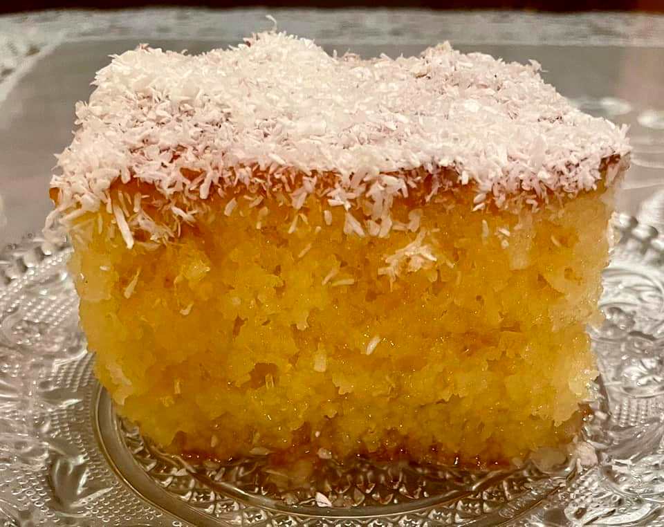 revaniIndokarido Ένα κομμάτι ραβανί σιροπιασμένο σε ένα πιάτο, πασπαλισμένο με λευκό ινδοκάρυδο.