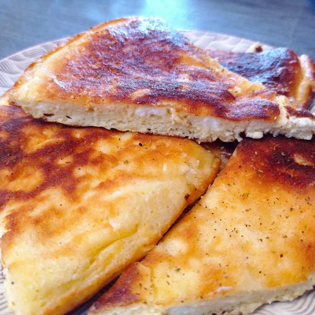 tiganopsomo Χρυσαφένια, στρογγυλή τυρόπιτα στο τηγάνι, κομμένη σε μερίδες.