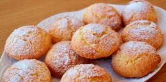 Ένα πιάτο γεμάτο με χρυσαφένια, στρογγυλά μπισκότα καρύδας, πασπαλισμένα με ζάχαρη άχνη, έτοιμα για σερβίρισμα.