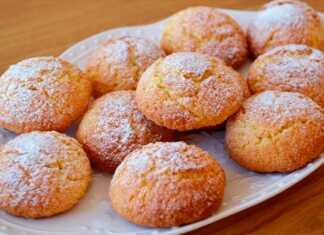 Ένα πιάτο γεμάτο με χρυσαφένια, στρογγυλά μπισκότα καρύδας, πασπαλισμένα με ζάχαρη άχνη, έτοιμα για σερβίρισμα.