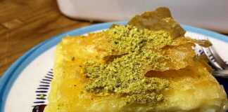 Ένα ταψί με λαχταριστή, χρυσαφένια σιροπιαστή μπουγάτσα με κρέμα τυριού, πασπαλισμένη με λίγα φιστίκια Αιγίνης, έτοιμη για σερβίρισμα.