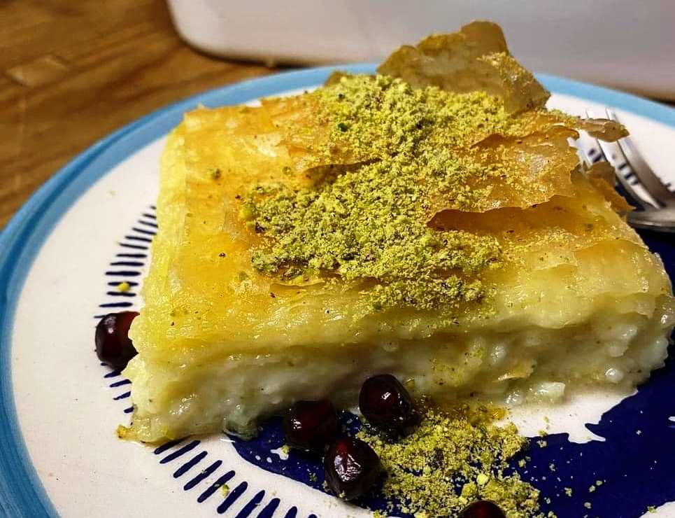 siropiasthMougatsa Ένα ταψί με λαχταριστή, χρυσαφένια σιροπιαστή μπουγάτσα με κρέμα τυριού, πασπαλισμένη με λίγα φιστίκια Αιγίνης, έτοιμη για σερβίρισμα.