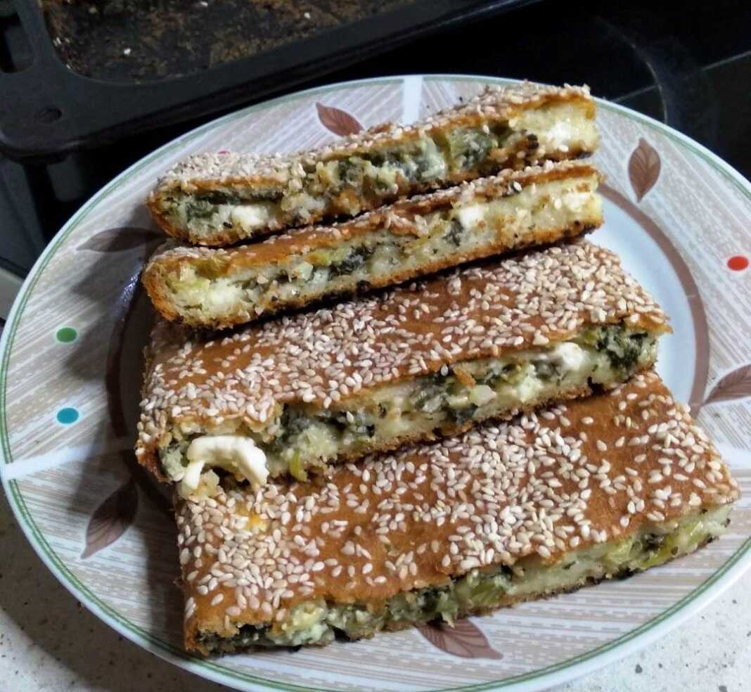 Σπανακόπιτα χωρίς φύλλο, ψημένη, πασπαλισμένη με σουσάμι, κομμένη σε τετράγωνα κομμάτια.