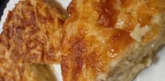 Ένα κομμάτι χρυσαφένιας κασερόπιτας χωρίς φύλλο σε ένα λευκό πιάτο. Η πίτα φαίνεται αφράτη και έχει τριμμένο κασέρι στην επιφάνεια.