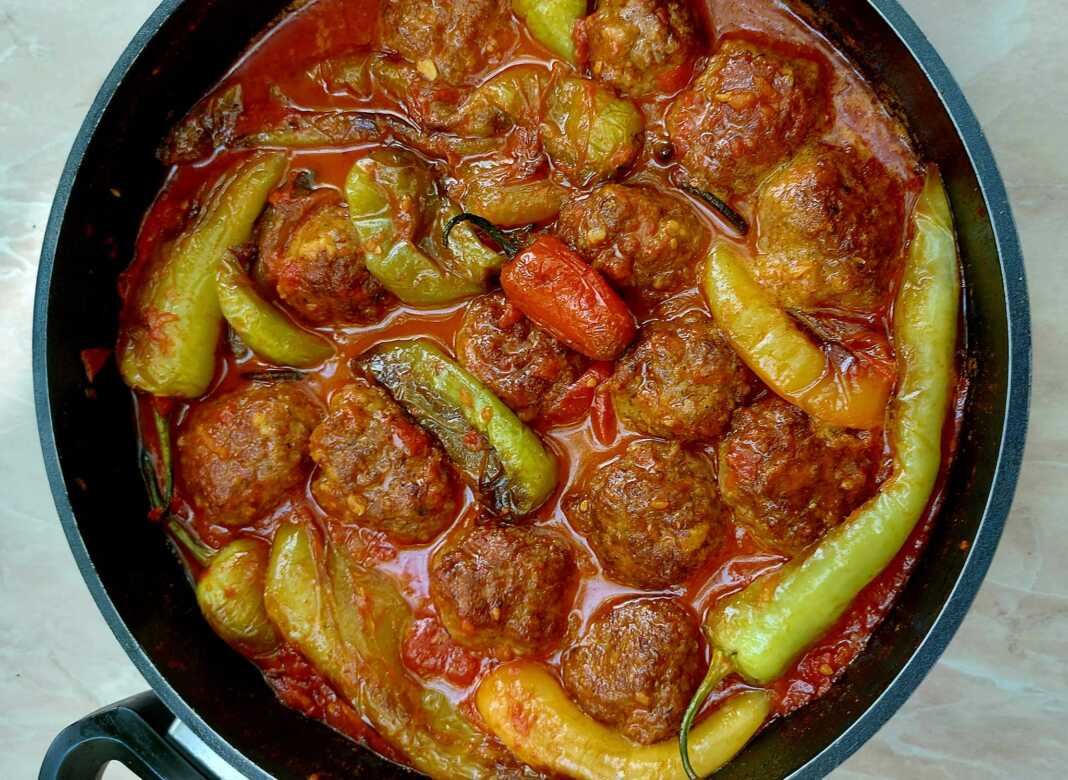 Μια κατσαρόλα γεμάτη με κεφτεδάκια και πιπεριές κέρατο μέσα σε πλούσια κόκκινη σάλτσα ντομάτας.