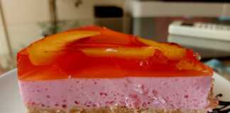 Ένα κομμάτι δροσερού cheesecake με μπισκοτένια βάση, λευκή κρέμα γιαουρτιού και δύο στρώσεις χρωματιστού ζελέ, γαρνιρισμένο με φέτες νεκταρινιού, σερβιρισμένο σε λευκό πιάτο.