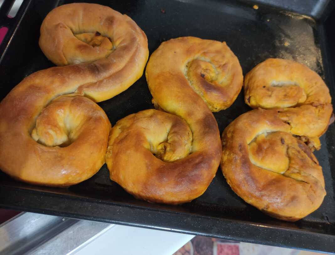 Τρεις κιμαδόπιτες σε σχήμα S τοποθετημένες σε ένα ταψί, με χρυσαφένιο χρώμα και λιωμένο βούτυρο στην επιφάνεια.