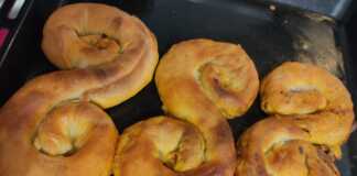 Τρεις κιμαδόπιτες σε σχήμα S τοποθετημένες σε ένα ταψί, με χρυσαφένιο χρώμα και λιωμένο βούτυρο στην επιφάνεια.