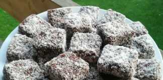 Ένα πιάτο γεμάτο με τετράγωνα γλυκάκια κέικ, καλυμμένα με σκούρα σοκολάτα και πασπαλισμένα με τριμμένη καρύδα.