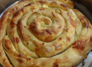 Στρογγυλή, χρυσαφένια ζυμωτή πίτα τοποθετημένη κυκλικά σε ταψί, γεμισμένη με φέτα και γιαούρτι, έτοιμη να κοπεί.