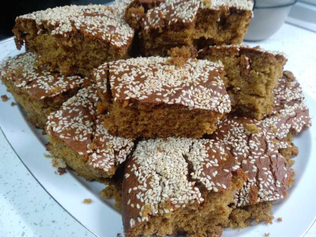 Μια φρεσκοψημένη, χρυσαφένια σταφιδόπιτα, πασπαλισμένη με σουσάμι, κομμένη σε κομμάτια, που αναδεικνύει τις ζουμερές σταφίδες στο εσωτερικό.