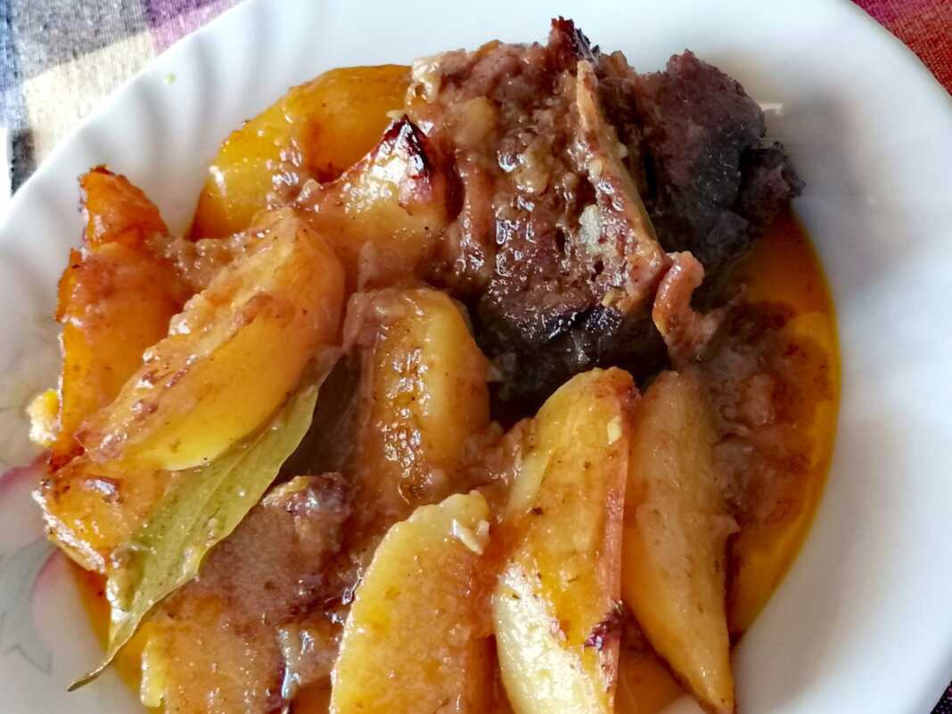 Ένα πιάτο με κοκκινιστή γίδα και πατάτες που ψήνονται στο φούρνο.