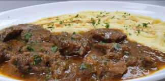 Ένα πιάτο με κομμάτια μοσχαρίσιου κρέατος με καφεκόκκινη σάλτσα, δίπλα σε έναν λευκό αφράτο πουρέ πατάτας, γαρνιρισμένο με φρέσκο μαϊντανό.