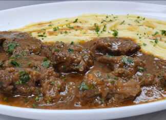 Ένα πιάτο με κομμάτια μοσχαρίσιου κρέατος με καφεκόκκινη σάλτσα, δίπλα σε έναν λευκό αφράτο πουρέ πατάτας, γαρνιρισμένο με φρέσκο μαϊντανό.