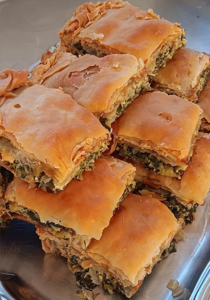 Μια ροδοψημένη, παραδοσιακή χωριάτικη σπανακοτυρόπιτα με τραγανό χειροποίητο φύλλο και σχηματισμένο κόθρο, χαραγμένη σε τετράγωνα κομμάτια μέσα στο ταψί