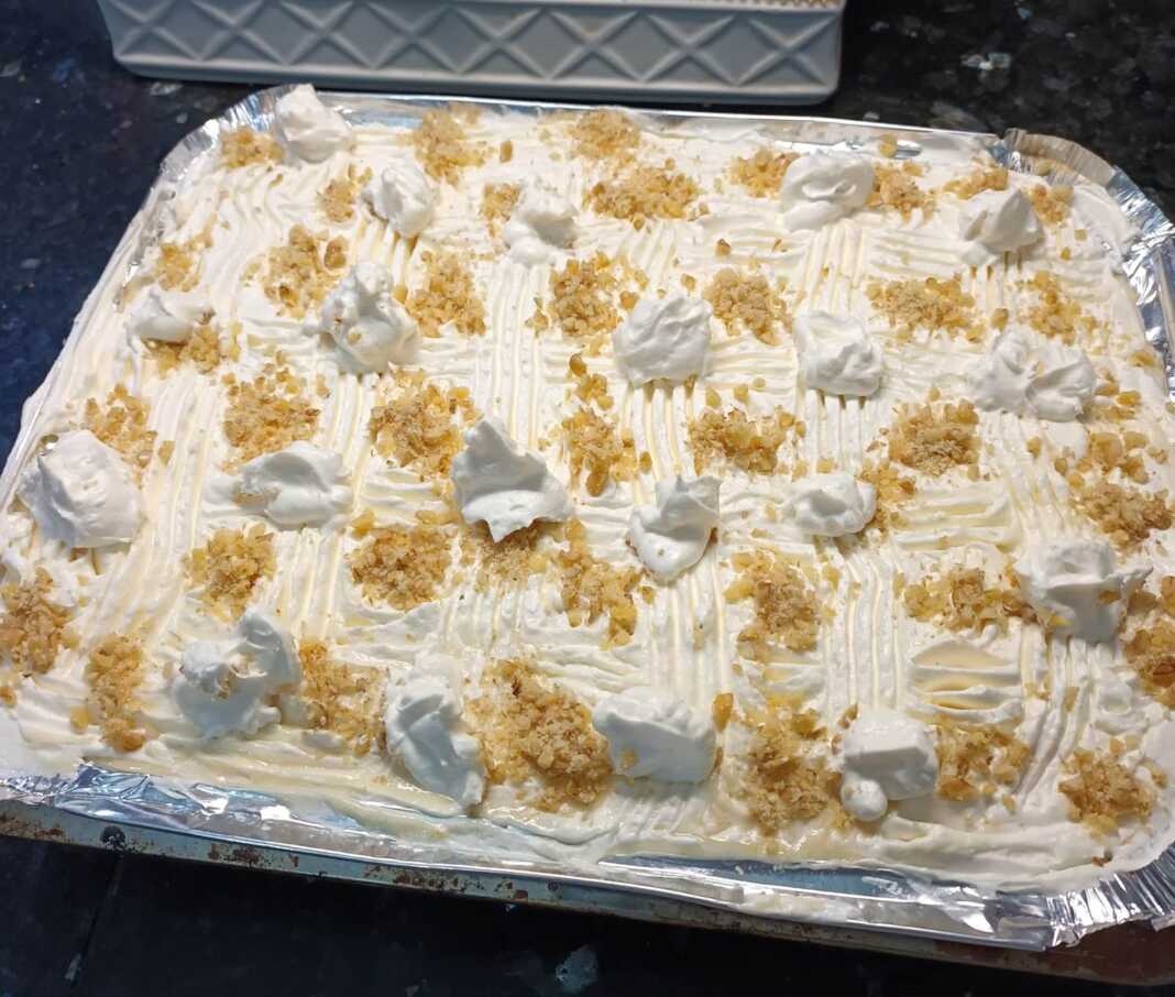 Ένα κομμάτι από ραβανί με στρώσεις κρέμας βανίλιας και σαντιγί, πασπαλισμένο με καρύδι.