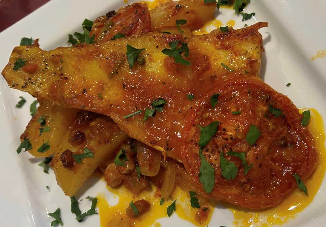 Ζουμερός μπακαλιάρος πλακί με πατάτες και πλούσια κόκκινη σάλτσα σε πιάτο.