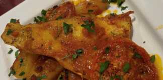 Ζουμερός μπακαλιάρος πλακί με πατάτες και πλούσια κόκκινη σάλτσα σε πιάτο.