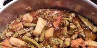 Μια κατσαρόλα γεμάτη με κοκκινιστό κοτόπουλο και μπάμιες σε πλούσια κόκκινη σάλτσα.