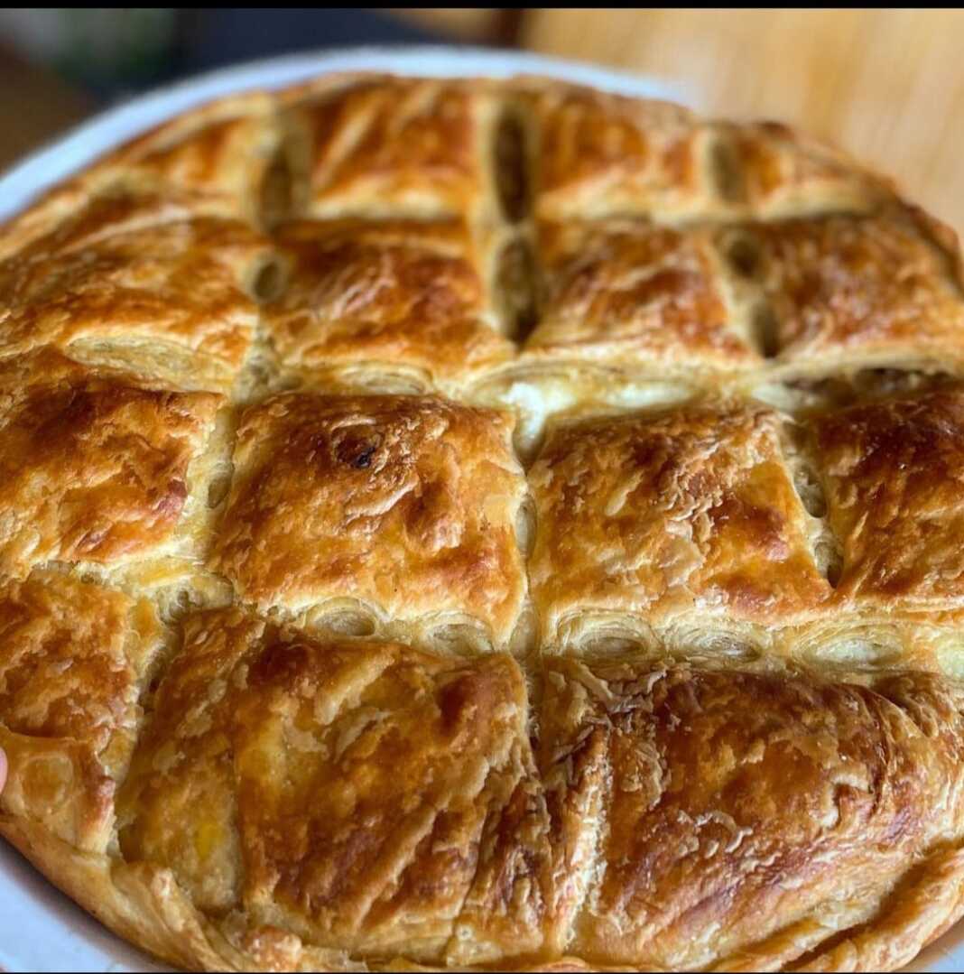 Μια στρογγυλή, χρυσαφένια πρασόπιτα με σπιτικό φύλλο, κομμένη σε κομμάτια, έτοιμη για σερβίρισμα.