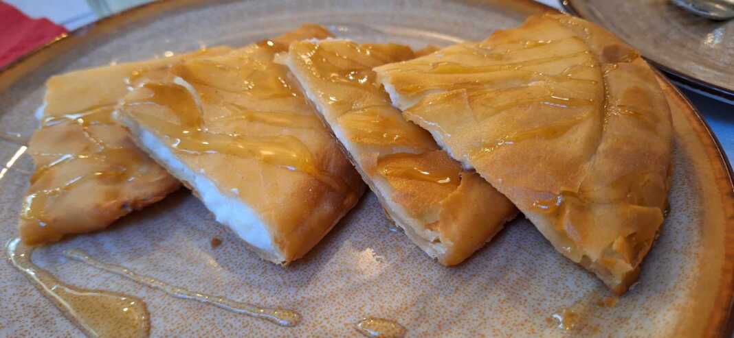 Πιάτο με μία Σφακιανή πίτα, περιχυμένη με μέλι και σουσάμι, έτοιμη να την απολαύσετε