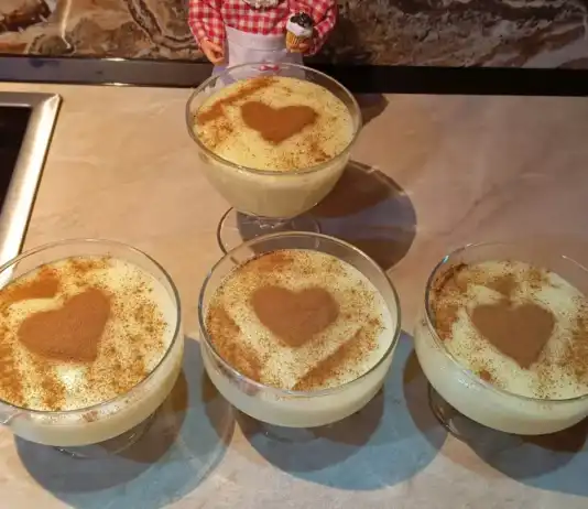 Λευκή, βελούδινη σπιτική κρέμα βανίλιας σε γυάλινο μπολ, πασπαλισμένη με κανέλα και διακοσμημένη με ένα κλωνάρι βανίλιας.