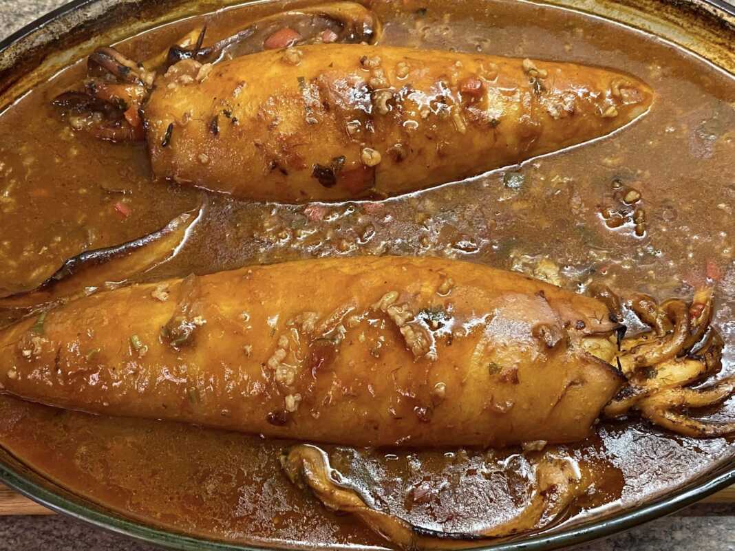 Προετοιμασία γεμιστών καλαμαριών σε ταψί, πριν το ψήσιμο, με πλούσια σάλτσα.