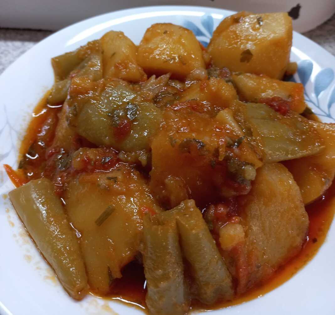 Ένα πιάτο με πατάτες γιαχνί και πολύχρωμα λαχανικά σε πλούσια κόκκινη σάλτσα.