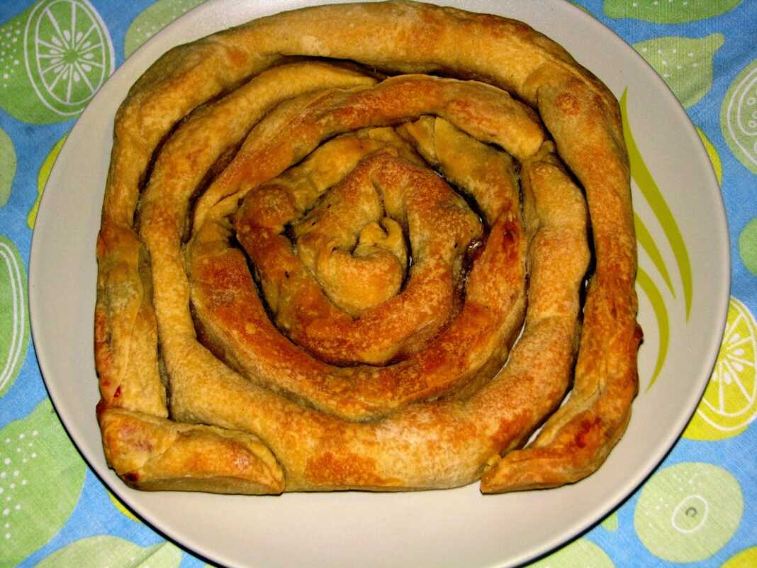 Παραδοσιακή στριφτή πίτα σαν σαλιγκάρι με ντομάτα και ελιές, ροδοκοκκινισμένη μέσα στο ταψί