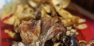 Ένα ταψί με λαχταριστό χρυσαφένιο αρνάκι και ψητές πατάτες, βγαλμένο από τον φούρνο, έτοιμο για σερβίρισμα.