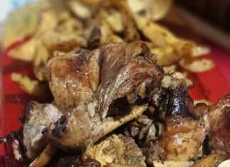 Ένα ταψί με λαχταριστό χρυσαφένιο αρνάκι και ψητές πατάτες, βγαλμένο από τον φούρνο, έτοιμο για σερβίρισμα.