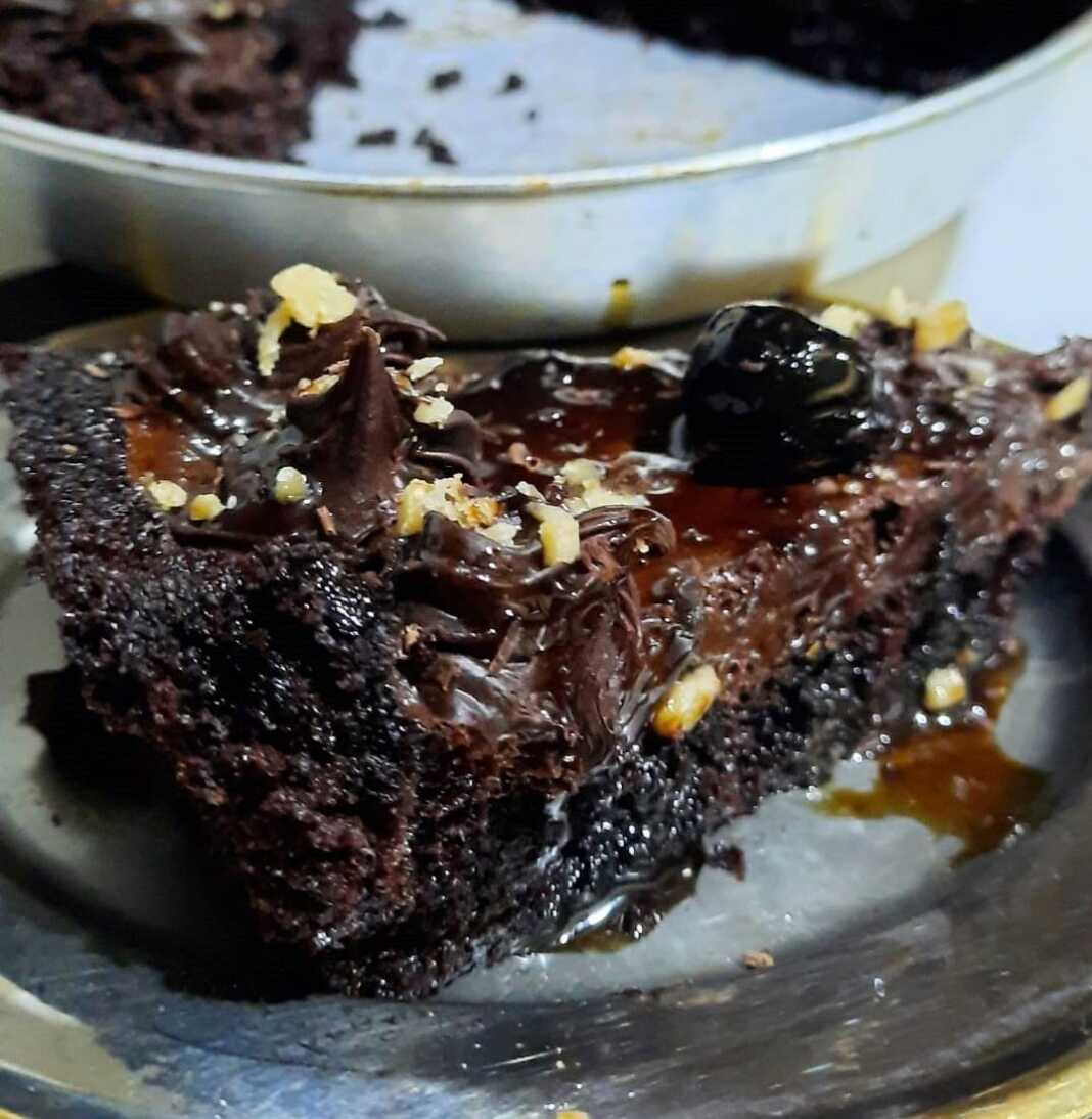 Μια φέτα από τάρτα σοκολάτας με πλούσια καφέ κρέμα, βάση παντεσπανιού και γαρνιρισμένη με λαμπερά κόκκινα βύσσινα.