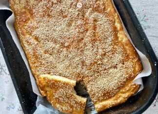 Μια χρυσαφένια και αφράτη τεμπελοτυρόπιτα πασπαλισμένη με σουσάμι μέσα σε ταψί με λαδόκολλα