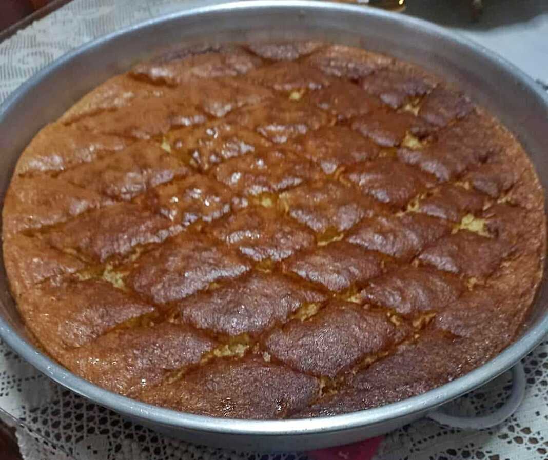 Ένα ταψί από σιροπιαστή Μελαχρινή με τριμμένο καρύδι στην επιφάνεια, σερβιρισμένο σε λευκό πιάτο.