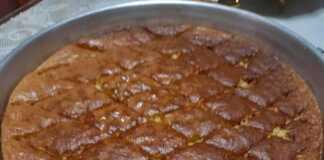 Ένα ταψί από σιροπιαστή Μελαχρινή με τριμμένο καρύδι στην επιφάνεια, σερβιρισμένο σε λευκό πιάτο.