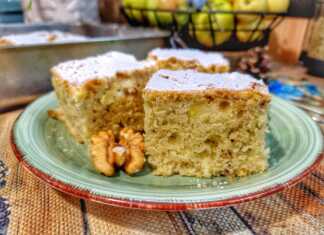 Ένα καλοψημένο κέικ μήλου σε ταψί πασπαλισμένο με άχνη ζάχαρη και γεμάτο κομμάτια από φρέσκα μήλα και χοντροκομμένα καρύδια