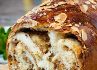 Μια χρυσαφένια πλεξούδα κέικ με ξηρούς καρπούς πασπαλισμένη με φιλέ αμυγδάλου, με τις στρώσεις καρυδιού να φαίνονται στο εσωτερικό