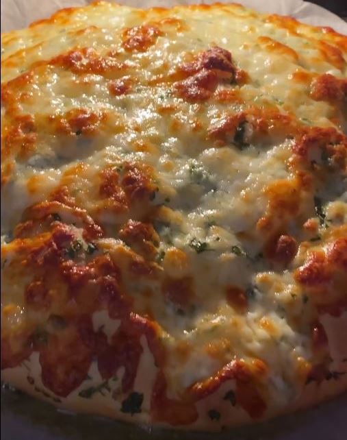 Μια ολόκληρη, χρυσαφένια σκορδόπιτα με λιωμένο τυρί και ψιλοκομμένο μαϊντανό από πάνω, τοποθετημένη σε ταψί με λαδόκολλα.