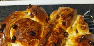 Ένα αφράτο, χρυσαφένιο τσουρέκι πλεγμένο σε πλεξούδα, με κομματάκια σοκολάτας στην επιφάνεια, σε ένα στρογγυλό ταψί με λαδόκολλα.