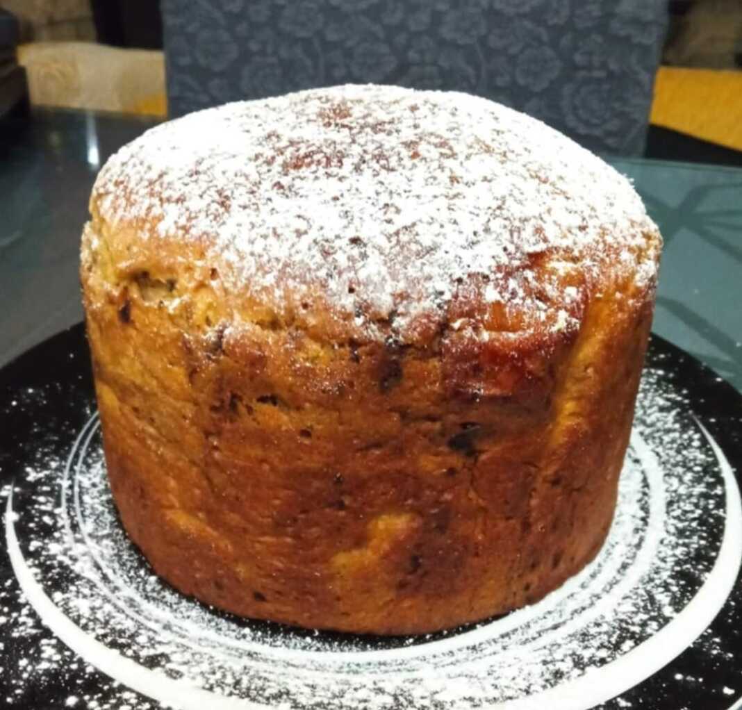 pantone Ένα ψηλό, στρογγυλό πανετόνε με ροδισμένη, γυαλιστερή επιφάνεια, διακοσμημένο με λιωμένη σοκολάτα, τοποθετημένο σε χάρτινη φόρμα.