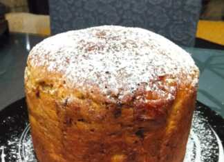 Ένα ψηλό, στρογγυλό πανετόνε με ροδισμένη, γυαλιστερή επιφάνεια, διακοσμημένο με λιωμένη σοκολάτα, τοποθετημένο σε χάρτινη φόρμα.