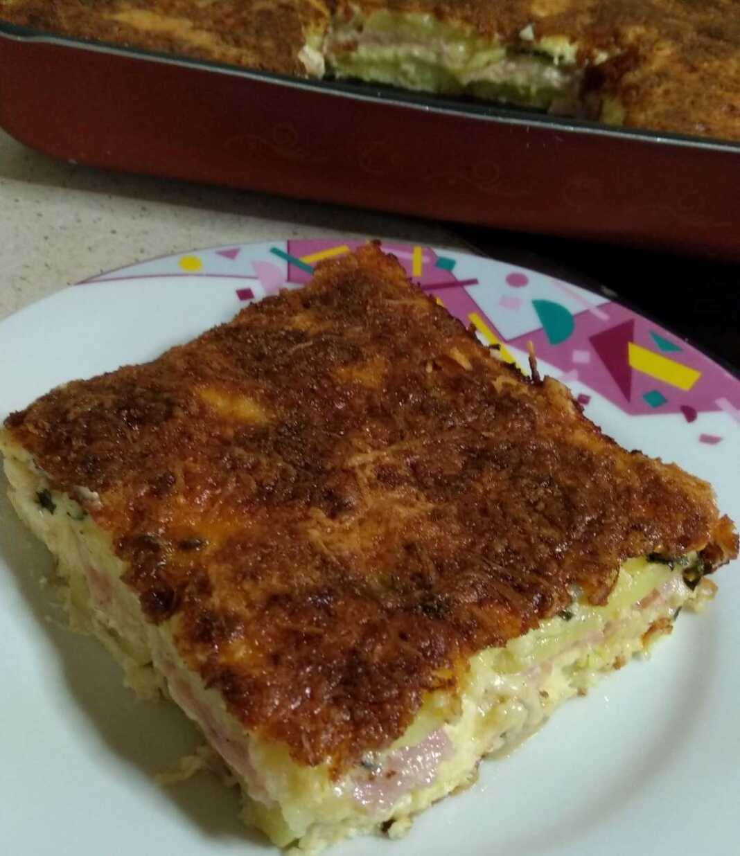 Ενα κομμάτι με χρυσαφένιες Πατάτες Ογκρατέν, με λιωμένο τυρί και φέτες πατάτας, έτοιμο για σερβίρισμα.