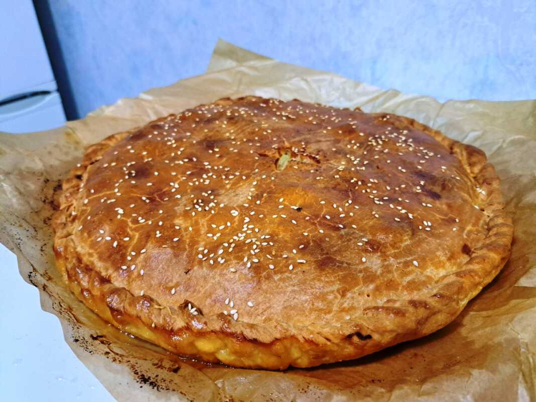 Χρυσαφένια πίτα με γαλοπούλα και πατάτες μέσα σε στρογγυλό ταψί, πασπαλισμένη με σουσάμι.