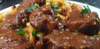 Ένα πιάτο λαχταριστής κερκυραϊκής παστιτσάδας με κομμάτια μοσχαριού και πλούσια κόκκινη σάλτσα, πασπαλισμένη με τριμμένο τυρί.